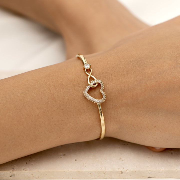Gioiello elegante in oro con cuore incastonato di pietre brillanti e dettaglio infinity.

