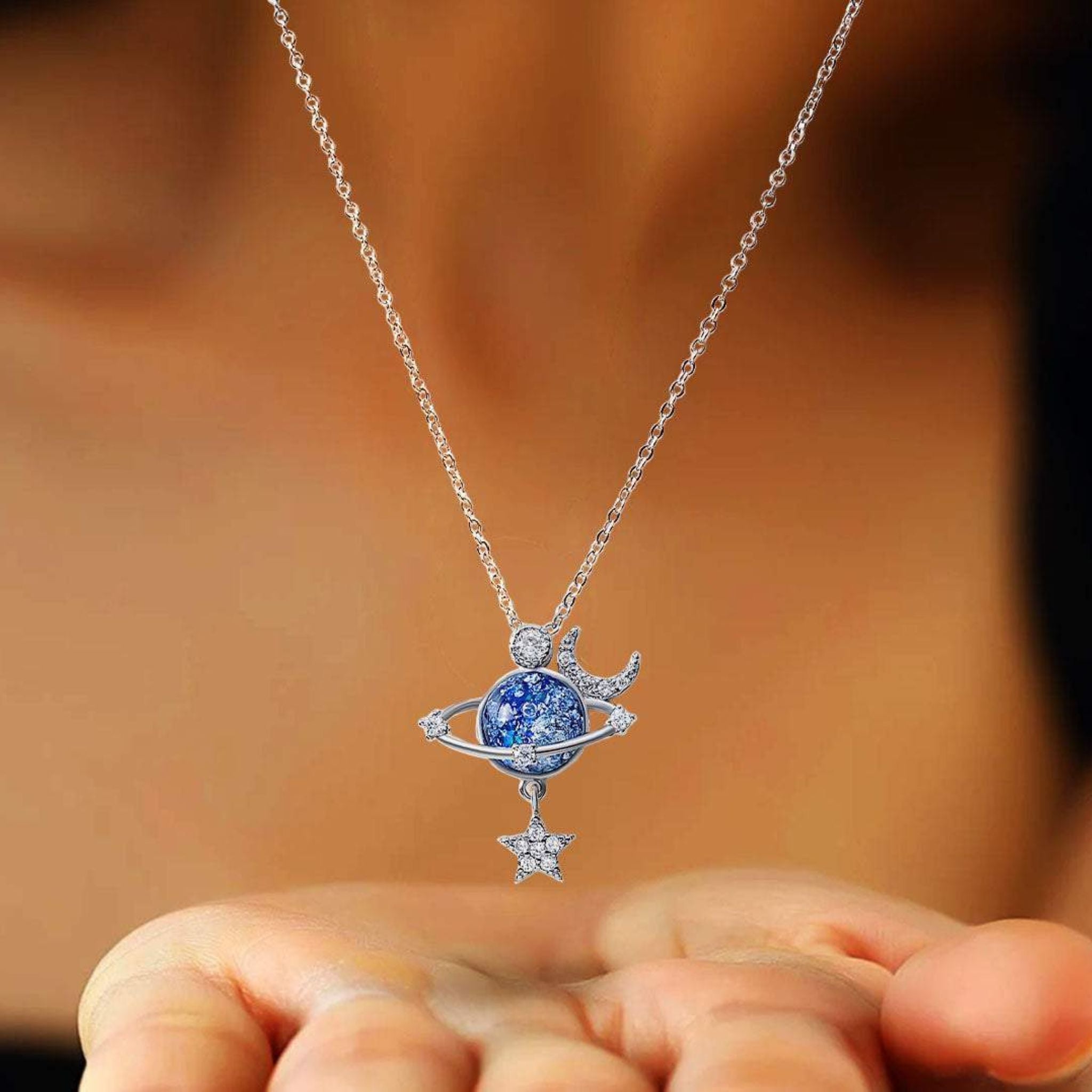 Ciondolo spaziale in argento con sfumature blu e decorazioni a tema luna e stelle.

